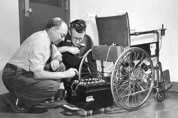 A first prototype of the Klein chair shown. With George Klein, on the left, pointing to a battery, and his colleague Robert Owens on the right looking at the battery.