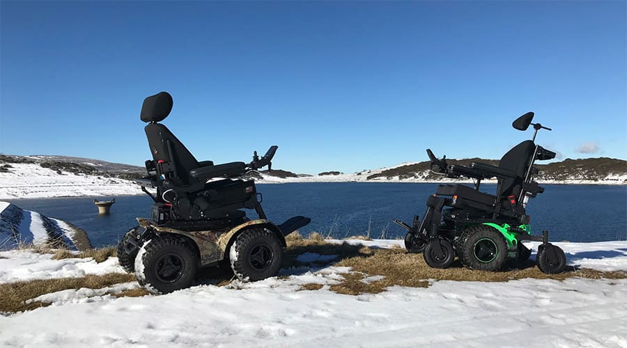 Two power wheelchairs in snow near a lake