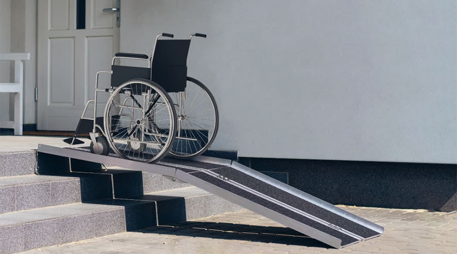 A ramp on a three-step stair with a wheelchair on the top part 