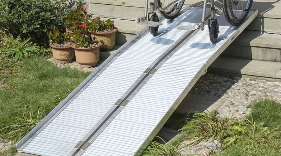 Portable wheelchair ramp installed on a three-step stair with plant pots at the side