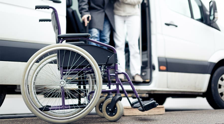 Two individuals at the door of a used mobility van and a wheelchair near the van