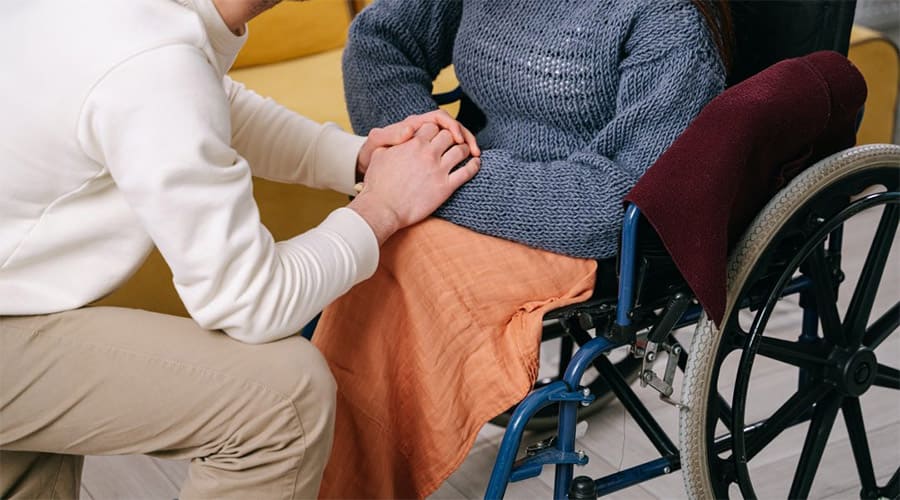 A person whose hands are on top of the hands of a woman in a wheelchair