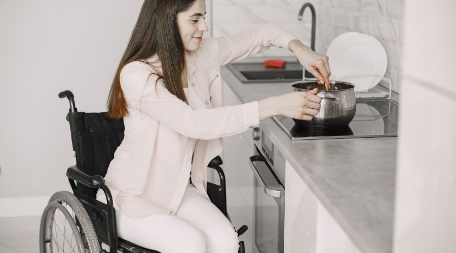 A woman in a wheelchair in the kitchen cooking